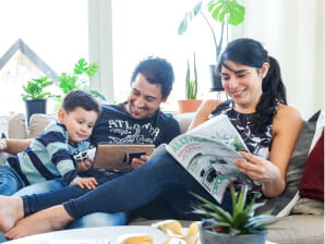 Familj sitter i soffa och tittar på surfplatta och läser tidning